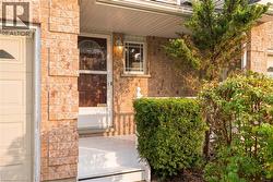 Welcoming front entrance featuring warm brick exterior, covered entry porch with railings, paneled door with sidelights, and mature landscaping including boxwood hedges and climbing ivy - 