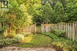 Private fenced yard featuring a wooden picket fence, lush perimeter plantings, and a decorative garden gate - 
