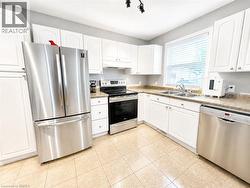 Kitchen featuring white cabinetry, stainless steel appliances, a double basin sink, and tile flooring -