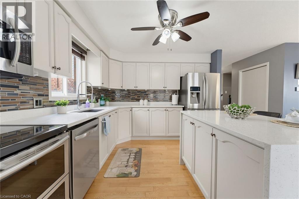 White cabinetry with dark hardware, stone-finish countertops, stainless steel appliances, wood-finish flooring, and a multi-tone tile backsplash - 592 Little Dover Crescent, Waterloo, ON - Indoor Photo Showing Kitchen With Upgraded Kitchen
