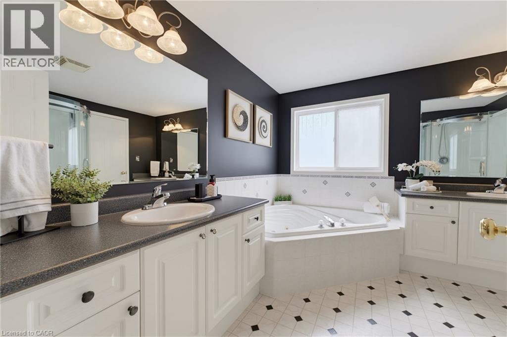 Dual vanity with integrated sinks, built-in corner soaking tub, white cabinetry, large vanity mirrors, and patterned floor tile - 592 Little Dover Crescent, Waterloo, ON - Indoor Photo Showing Bathroom