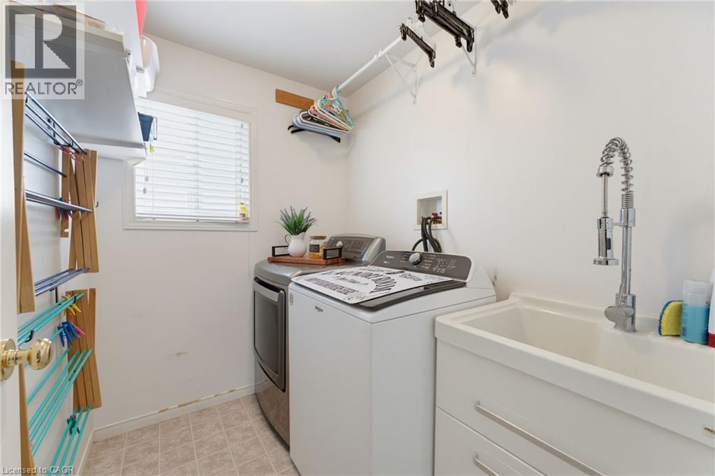 White utility sink with a chrome pull-down faucet, accompanied by a window with blinds and light-toned tile flooring - 592 Little Dover Crescent, Waterloo, ON - Indoor Photo Showing Laundry Room