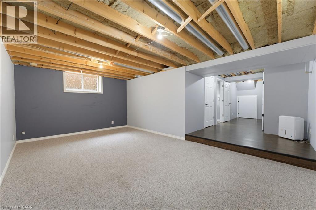 Unfinished ceiling with exposed joists, carpeted flooring, window, and a raised platform with wood-finish flooring - 592 Little Dover Crescent, Waterloo, ON - Indoor Photo Showing Basement