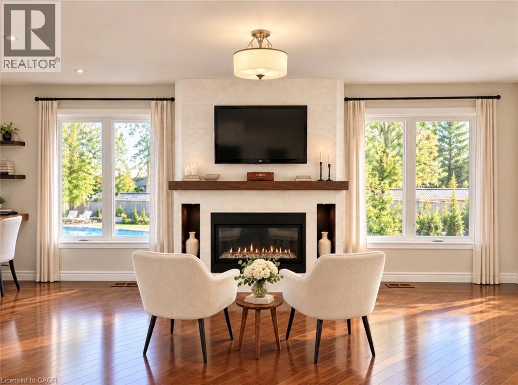 Hardwood flooring, fireplace with stone surround, wood mantel, recessed shelving, and two large windows - 56 Windrush Trail, Kitchener, ON