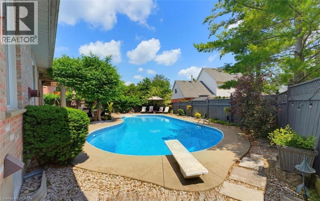 Curved in-ground pool with concrete surround, diving board, and stone paver patio - 56 Windrush Trail, Kitchener, ON