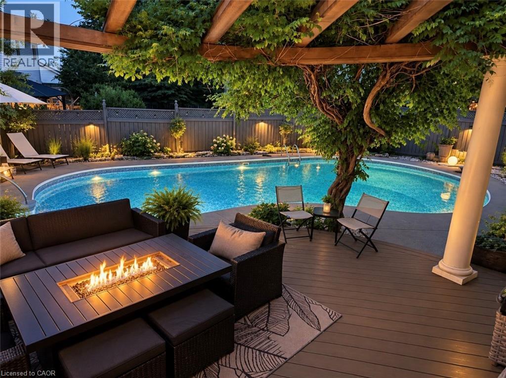 Curved inground pool, expansive wood-finish deck, integrated outdoor lighting, wood pergola with mature foliage, and built-in fire pit - 56 Windrush Trail, Kitchener, ON
