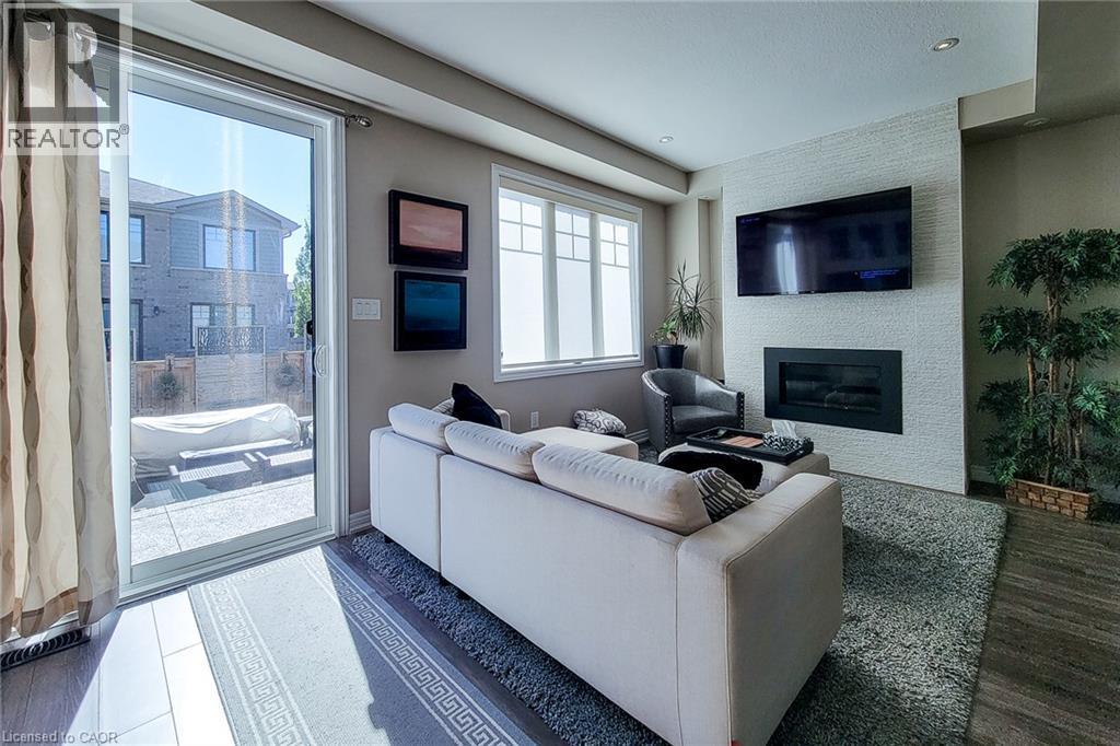 Sliding glass patio doors, built-in electric fireplace, textured accent wall, recessed lighting, and wood-finish flooring - 65 Waterview Lane, Grimsby, ON