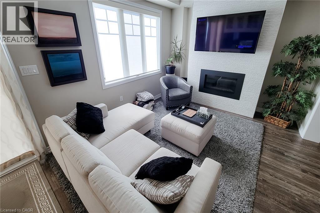 Modern fireplace with textured surround, integrated television mount, and wood-finish flooring - 65 Waterview Lane, Grimsby, ON
