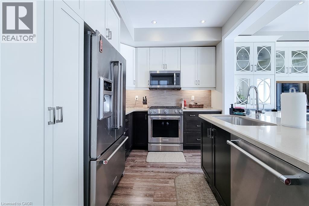 Stainless steel appliances, white and dark wood-finish cabinetry, light-toned countertops, tile backsplash, and wood-finish flooring - 65 Waterview Lane, Grimsby, ON