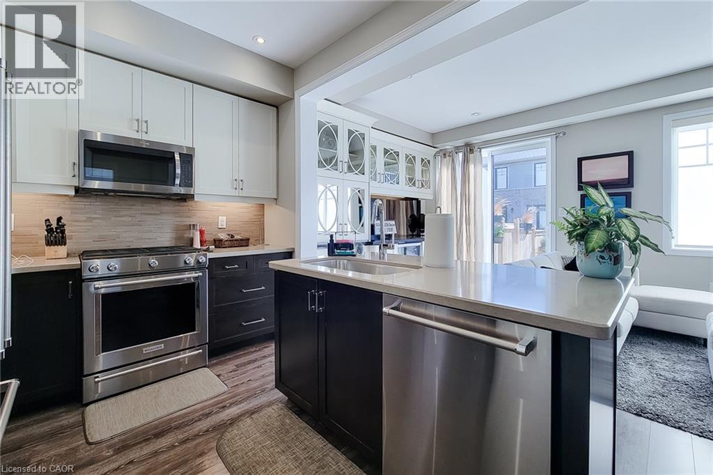 Modern kitchen featuring stainless steel appliances, a center island with an undermount sink, two-tone cabinetry, and wood-finish flooring - 65 Waterview Lane, Grimsby, ON