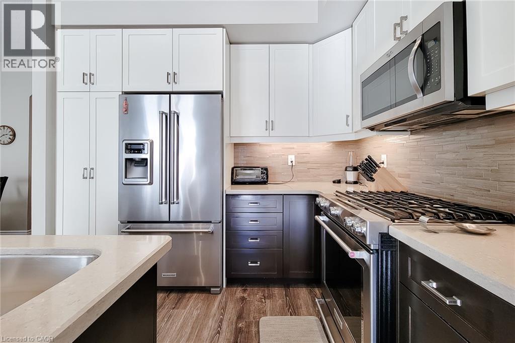 Stainless steel appliances, wood-finish flooring, white upper cabinetry, dark lower cabinetry, and light-toned countertops - 65 Waterview Lane, Grimsby, ON