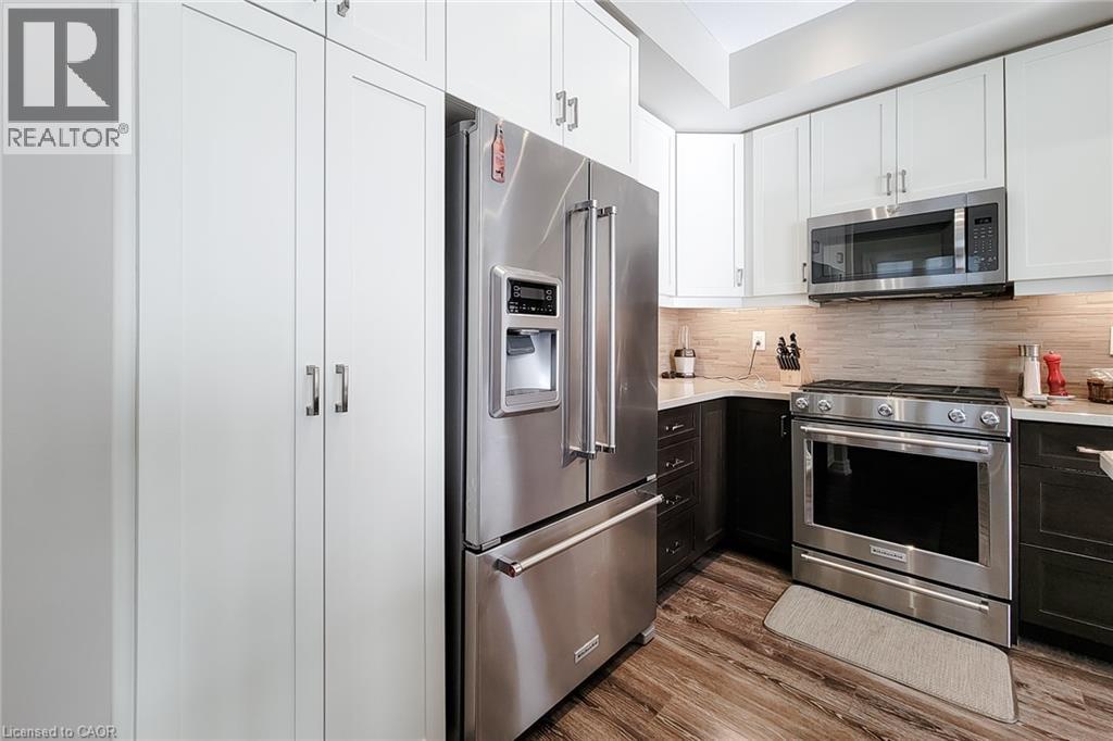 Stainless steel appliances, wood-finish flooring, two-tone cabinetry, light-toned backsplash, and white countertops - 65 Waterview Lane, Grimsby, ON