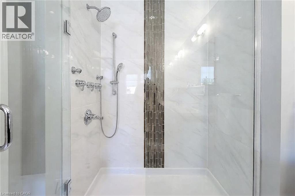 Glass-enclosed shower with a rainfall showerhead, handheld sprayer, multiple body jets, and a decorative tile accent band - 65 Waterview Lane, Grimsby, ON