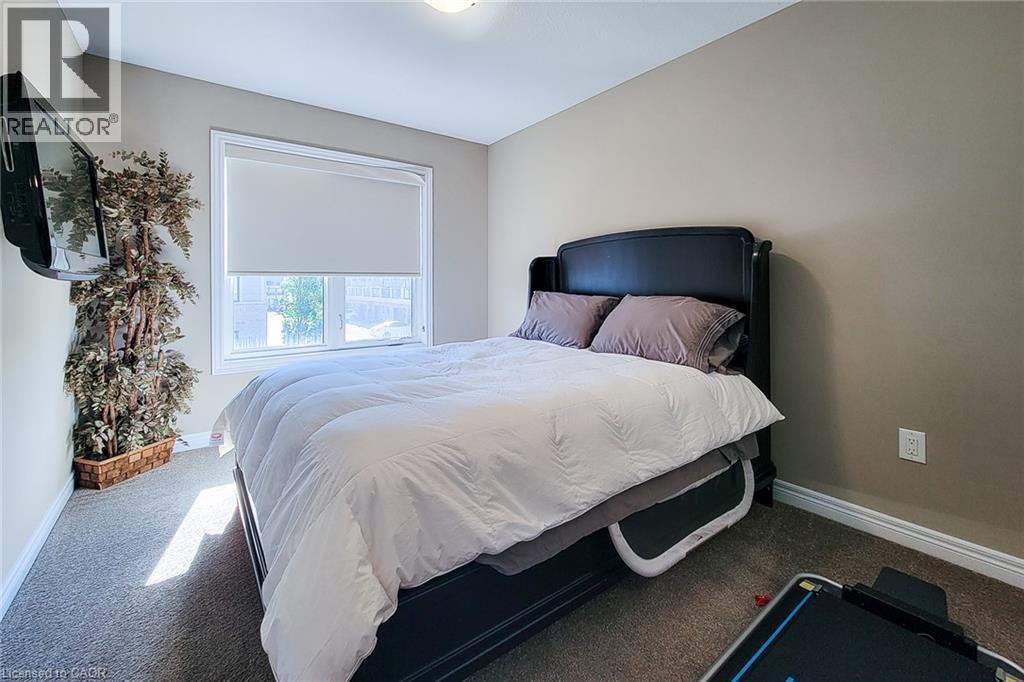 Wall-mounted television fixture, window with roller shade, neutral wall paint, and gray carpet flooring - 65 Waterview Lane, Grimsby, ON