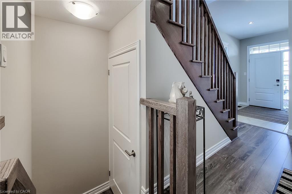 Wood-finish flooring, dark wood staircase with spindle railing, white interior door, and a front entry door with transom window - 65 Waterview Lane, Grimsby, ON