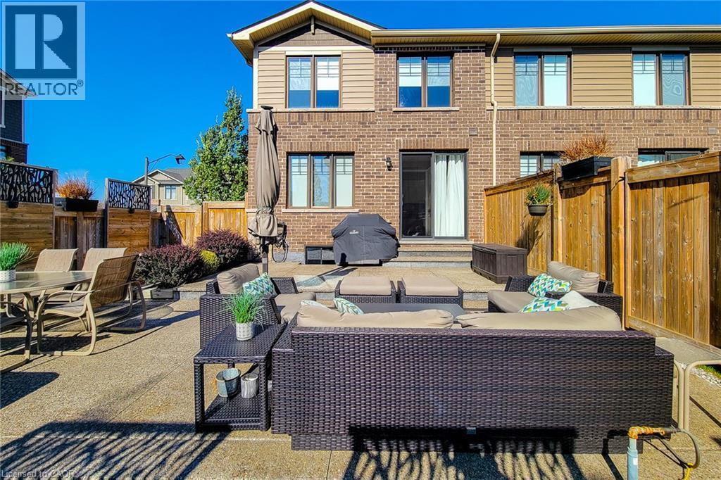 Expansive stone patio with a brick and siding exterior, featuring a sliding glass door and fenced perimeter - 65 Waterview Lane, Grimsby, ON