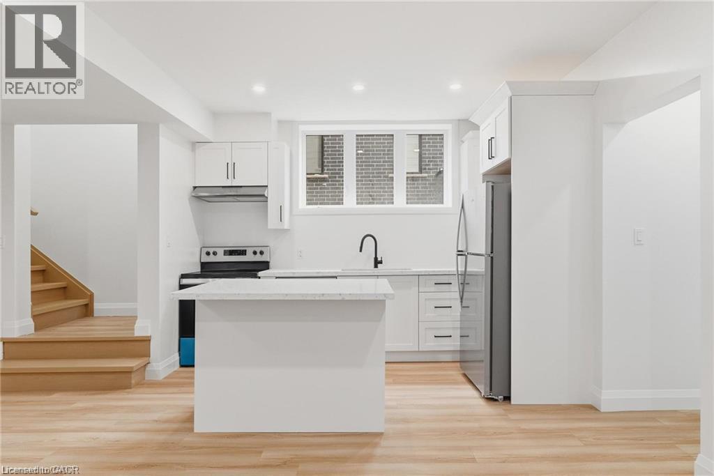 Open-concept kitchen with wood-finish flooring, white cabinetry, integrated appliances, and a central island with a light-toned countertop - 36 Elliott Street Unit# 1, Cambridge, ON