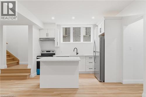 Open-concept kitchen with wood-finish flooring, white cabinetry, integrated appliances, and a central island with a light-toned countertop - 36 Elliott Street Unit# 1, Cambridge, ON 
