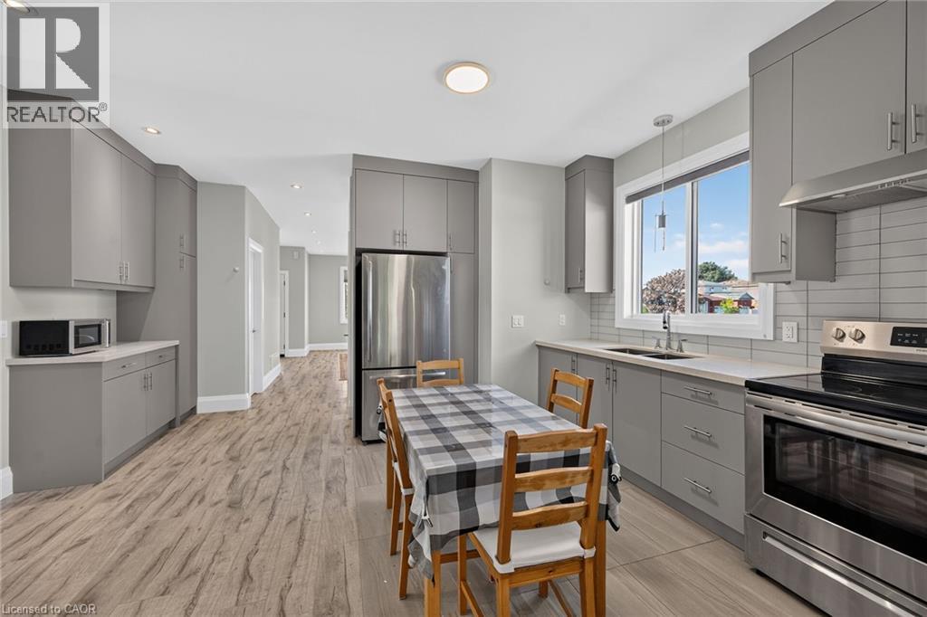 Contemporary kitchen featuring grey cabinetry, stainless steel appliances, light-toned countertops, and wood-finish flooring - 41 Eleanor Avenue, Hamilton, ON