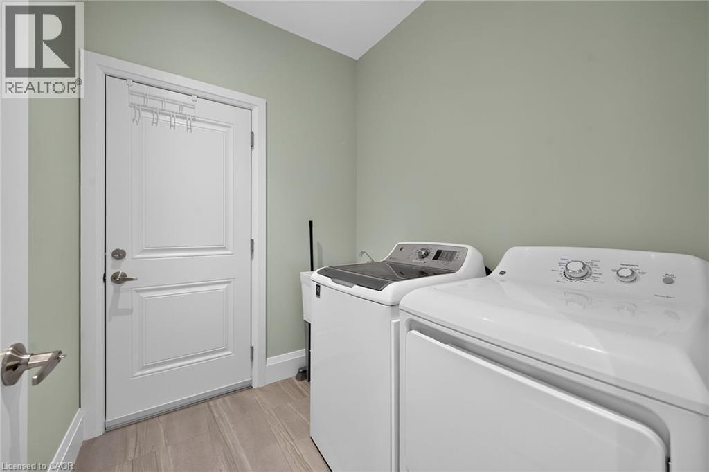 Laundry area featuring light green walls, a white paneled door with brushed nickel hardware, and wood-finish flooring - 41 Eleanor Avenue, Hamilton, ON