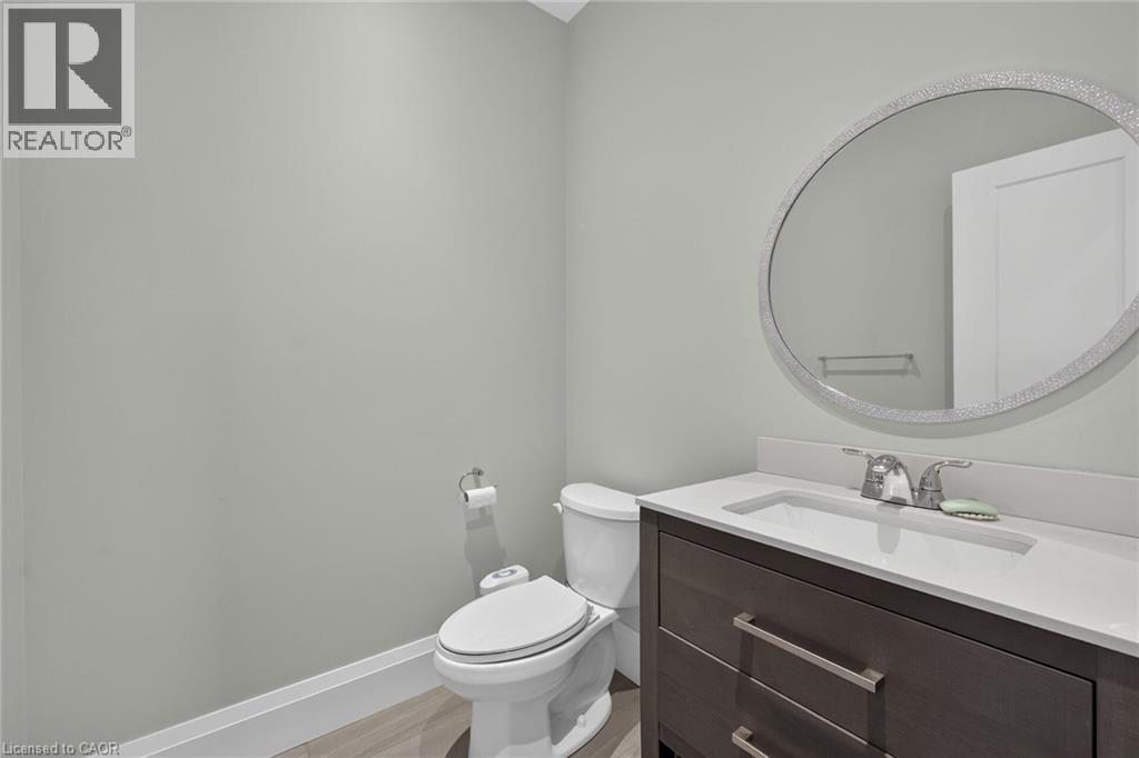 Vanity with integrated sink, stone countertop, wood-finish cabinetry, and a circular wall mirror - 41 Eleanor Avenue, Hamilton, ON
