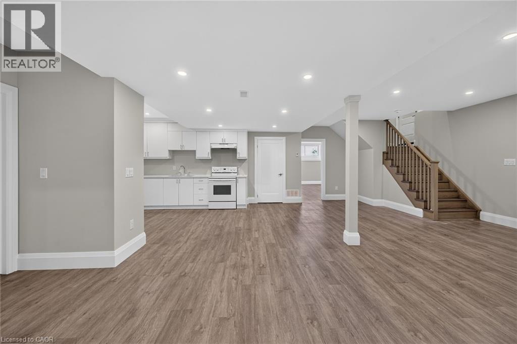 Open-concept area featuring wood-finish flooring, recessed lighting, a full kitchen with white cabinetry and appliances, and a wood staircase - 41 Eleanor Avenue, Hamilton, ON
