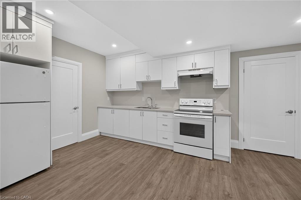 Kitchenette featuring wood-finish flooring, white cabinetry, integrated stainless steel appliances, a stainless steel sink, and recessed lighting - 41 Eleanor Avenue, Hamilton, ON