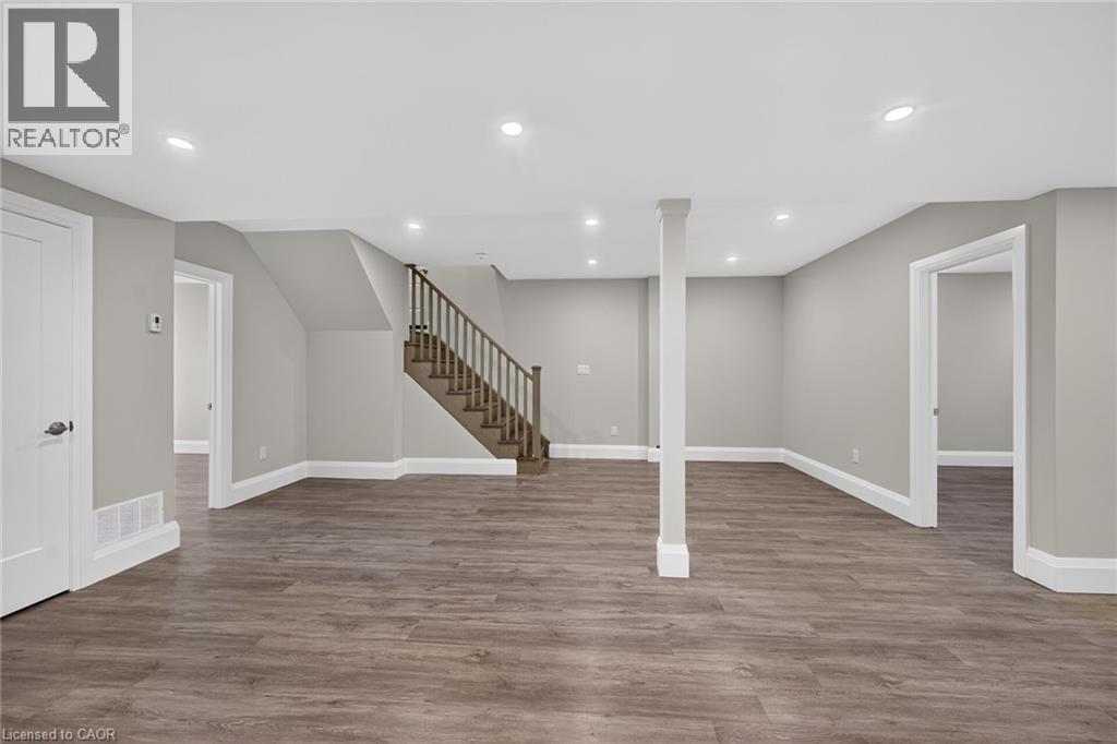 Spacious finished room with wood-finish flooring, recessed lighting, and a prominent staircase with wood railings - 41 Eleanor Avenue, Hamilton, ON