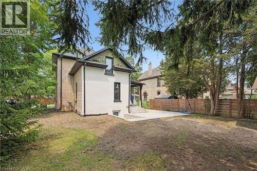 Exterior featuring a neutral stucco finish, dark framed windows, a gabled roofline, a concrete patio, and a wood fence - 245 Lowther Street S, Cambridge, ON 