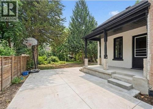Rear concrete patio with a covered porch, wood-paneled fence, and mature trees - 245 Lowther Street S, Cambridge, ON 