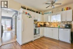Wood-finish flooring, white cabinetry, dark countertops, a tiled backsplash, and an overhead ceiling fan -