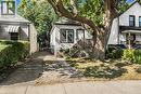 White siding exterior with black trim, a mature shade tree, a concrete pathway, a wooden porch with railing, and a striped window awning - 29 Wexford Avenue N, Hamilton, ON 