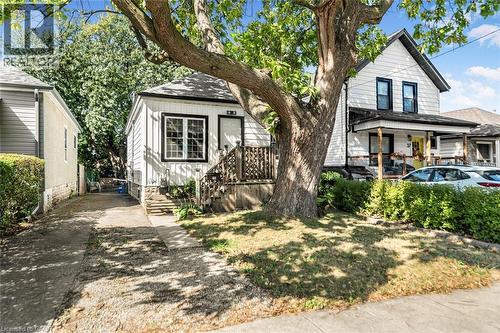 White siding exterior with a dark trim, covered front porch, and a mature front yard tree - 29 Wexford Avenue N, Hamilton, ON 