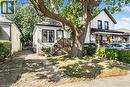White siding exterior with a dark trim, covered front porch, and a mature front yard tree - 29 Wexford Avenue N, Hamilton, ON 