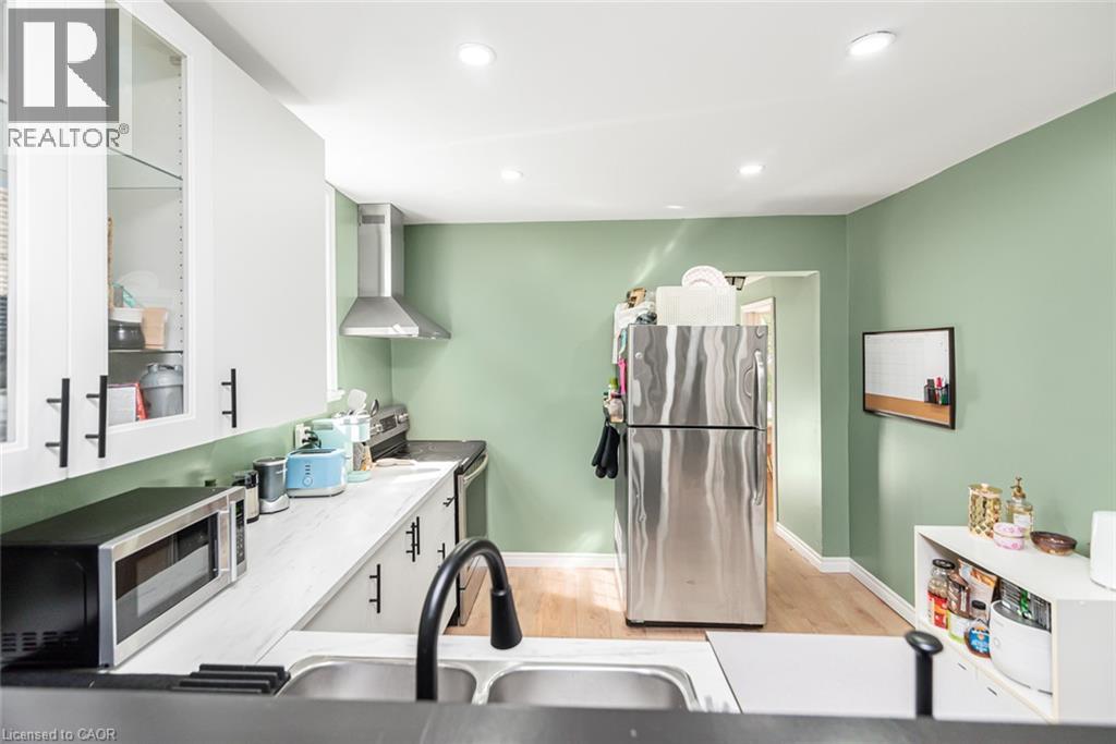Kitchen featuring white cabinetry, stainless steel appliances, recessed lighting, wood-finish flooring, and a stainless steel sink with a matte black faucet - 29 Wexford Avenue N, Hamilton, ON