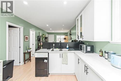 White cabinetry with black hardware, light wood-finish flooring, recessed lighting, and a stainless steel sink with a black faucet - 29 Wexford Avenue N, Hamilton, ON 