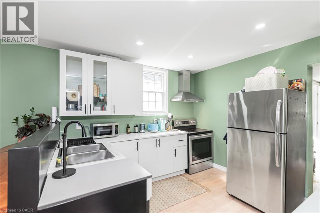 Kitchen featuring white cabinetry, stainless steel appliances, a double basin sink with a gooseneck faucet, and light wood-finish flooring - 29 Wexford Avenue N, Hamilton, ON