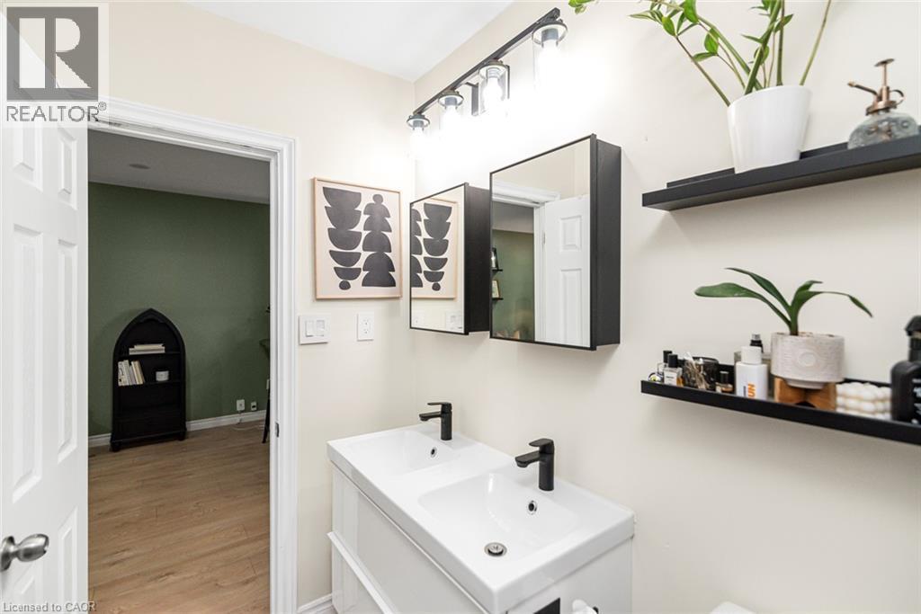 Dual white rectangular sinks with matte black faucets, wall-mounted mirrored medicine cabinets, and sleek black floating shelves - 29 Wexford Avenue N, Hamilton, ON