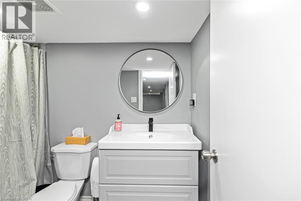 Vanity with built-in storage, circular framed mirror, white toilet, and recessed lighting - 29 Wexford Avenue N, Hamilton, ON