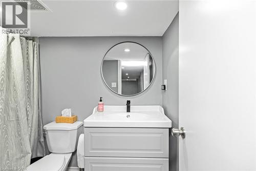 Vanity with built-in storage, circular framed mirror, white toilet, and recessed lighting - 29 Wexford Avenue N, Hamilton, ON 