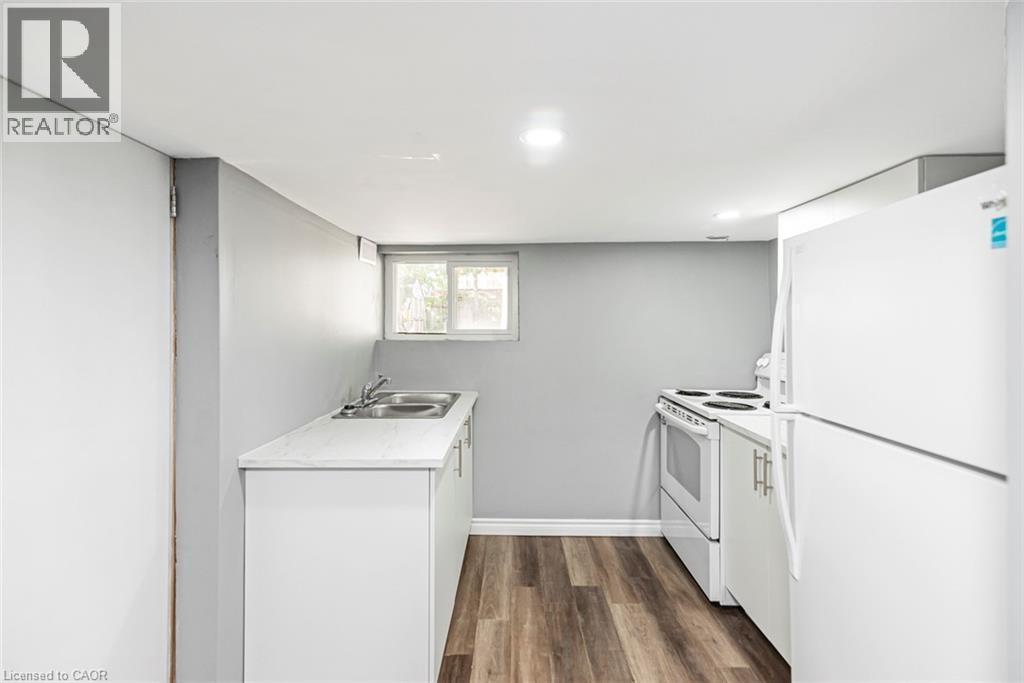 Compact kitchen area featuring wood-finish flooring, white cabinetry, a double basin sink, and a white electric range - 29 Wexford Avenue N, Hamilton, ON