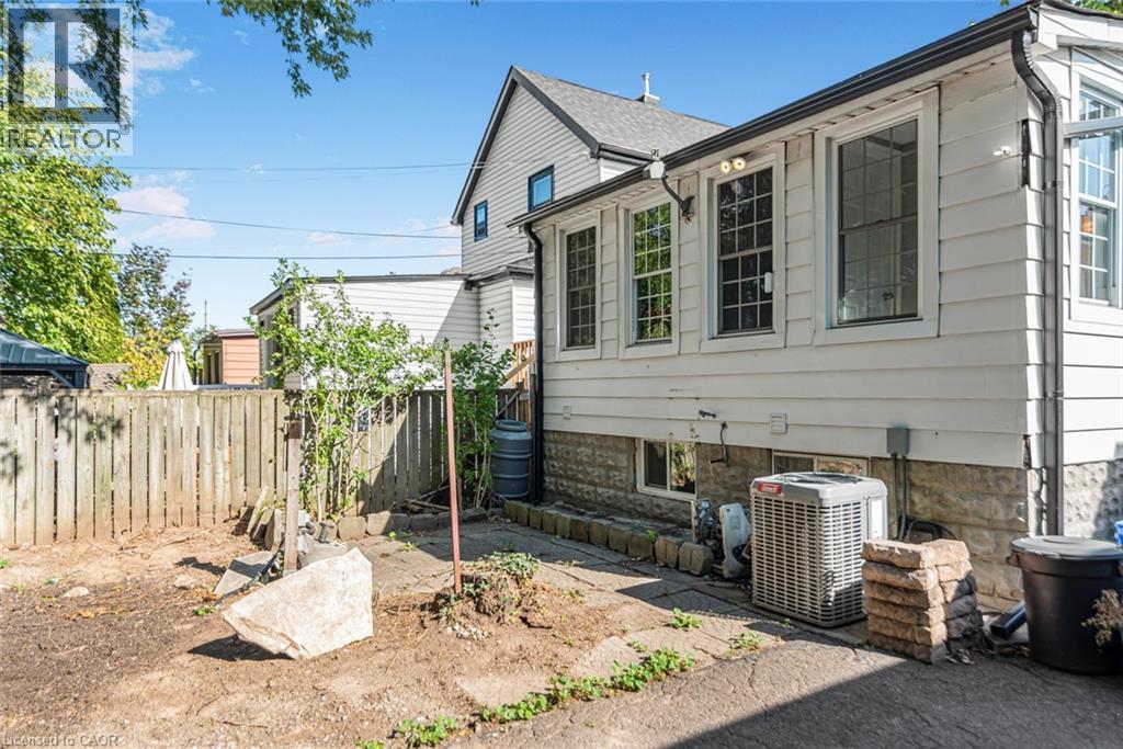 Exterior featuring white siding, a stone foundation, multiple windows, and an outdoor unit - 29 Wexford Avenue N, Hamilton, ON