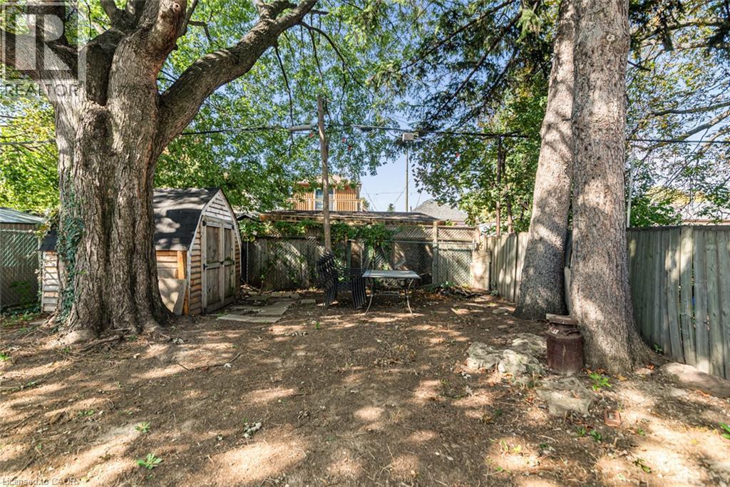 Expansive backyard featuring mature trees, a wooden storage shed, and a privacy fence - 29 Wexford Avenue N, Hamilton, ON