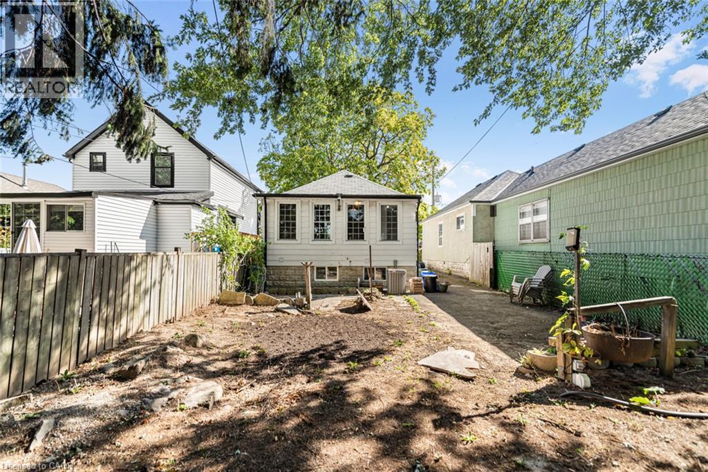 Rear exterior featuring white siding, a small addition with multiple windows, and a paved path - 29 Wexford Avenue N, Hamilton, ON