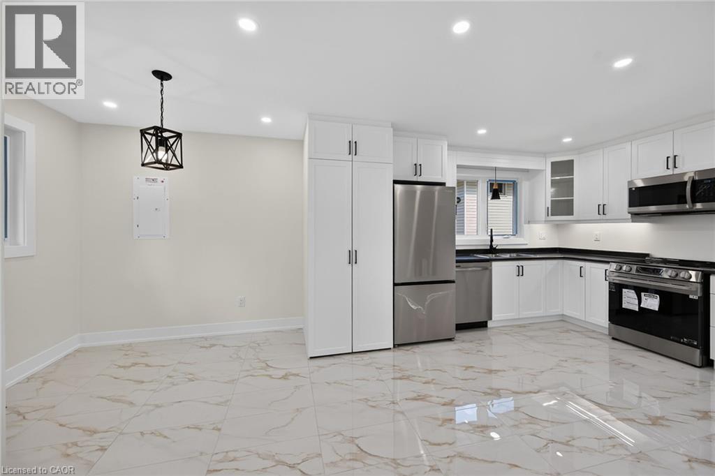 Kitchen featuring white cabinetry, stainless steel appliances, dark countertops, and white tile flooring - 331 East 17Th Street, Hamilton, ON