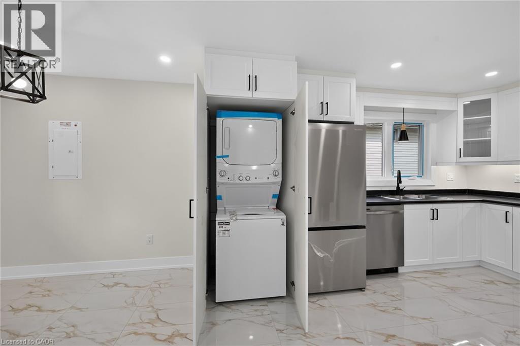 White shaker-style cabinetry with black hardware, stainless steel appliances, black countertops, and a stacked laundry unit - 331 East 17Th Street, Hamilton, ON