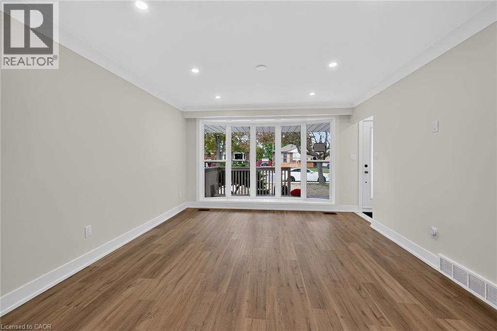 Spacious room featuring wood-finish flooring, recessed lighting, crown molding, and a prominent bay window - 331 East 17Th Street, Hamilton, ON