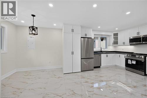 Kitchen featuring white cabinetry, stainless steel appliances, dark countertops, and white tile flooring - 331 East 17Th Street, Hamilton, ON 