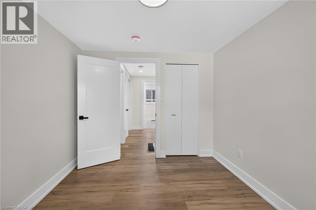 Wood-finish flooring, white bi-fold closet doors, white interior door with black hardware, recessed lighting, and light-toned wall finishes - 331 East 17Th Street, Hamilton, ON