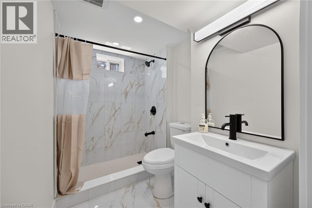 Bathroom featuring a white vanity with integrated sink, black hardware, arched mirror, and recessed lighting - 331 East 17Th Street, Hamilton, ON